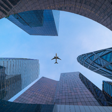 Photo taken looking up between modern skyscrapers and with a jet airliner flying overhead.